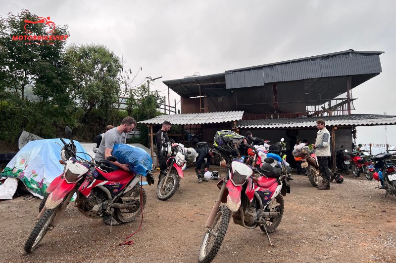 A group of adventure riders preparing their dirt bikes outside a rustic mountain lodge