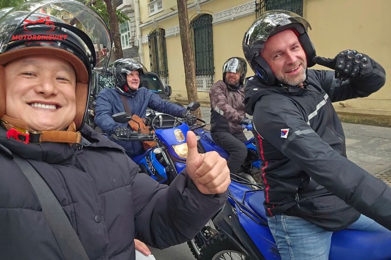 Four men wearing helmets posing on blue motorbikes on a city street